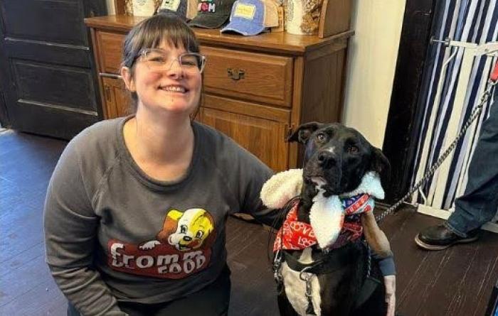 Smiling person kneeling on the floor next to a black and white dog